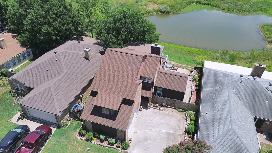 A brown shingle roof on a two-story home near a pond, seen at an angle from the air