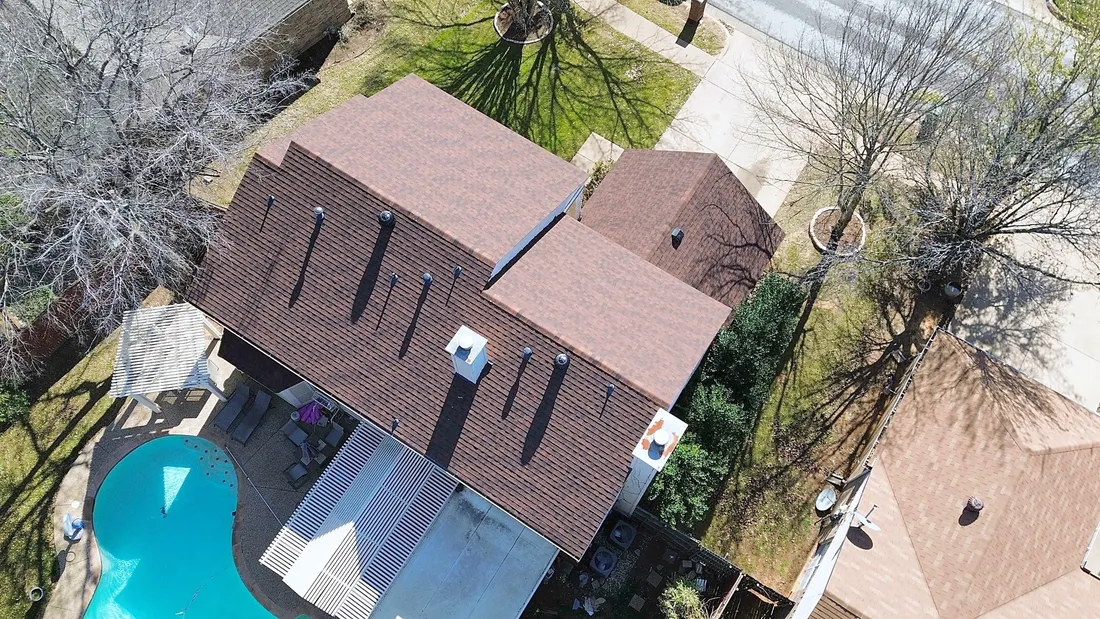 A brown shingle roof with turbine vents beside a backyard pool, from the air