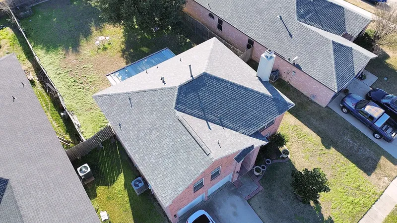 A gray shingle roof on a two-story brick home with a chimney, seen at an angle from the air