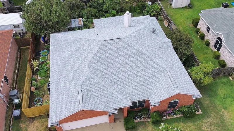 A light gray shingle roof on a red brick home with flower beds out front, from the air